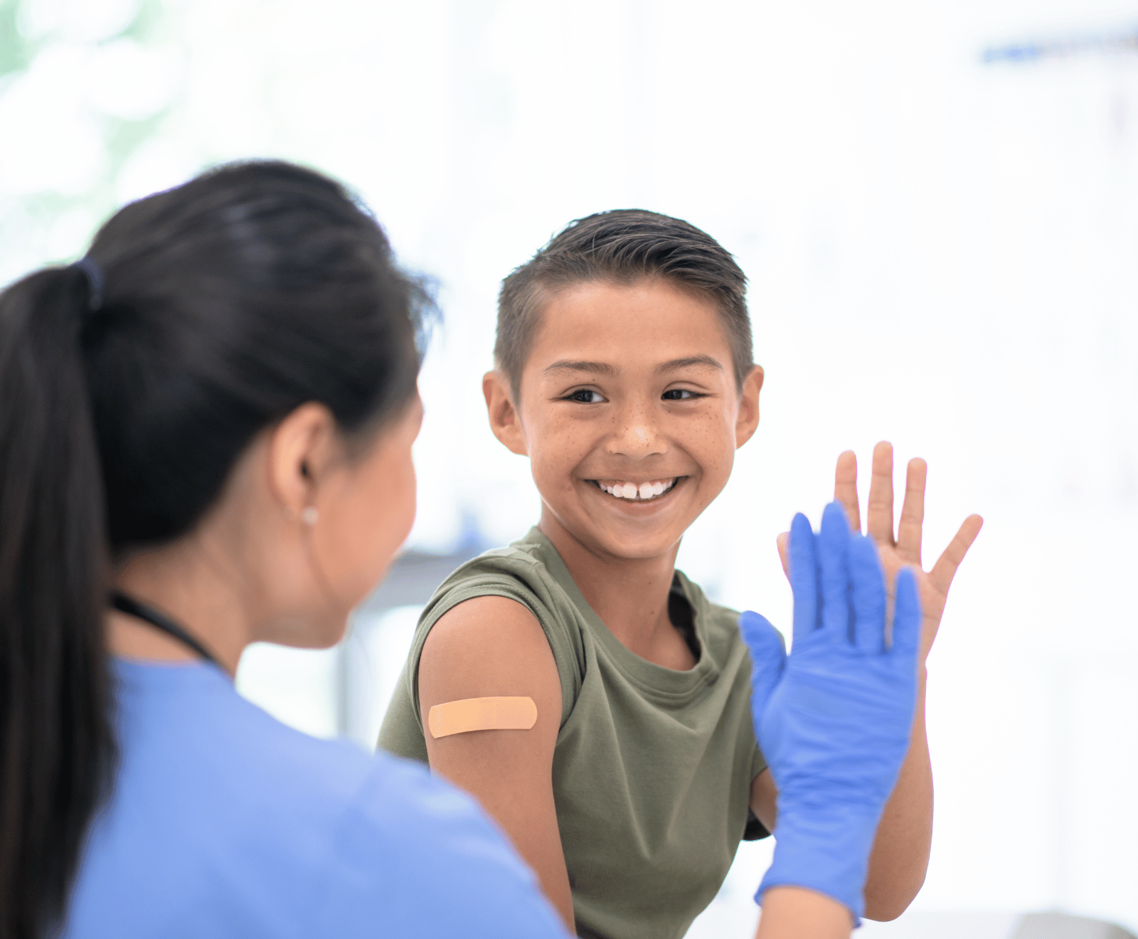 Boy with adhesive bandage on arm getting high fived by a medical worker